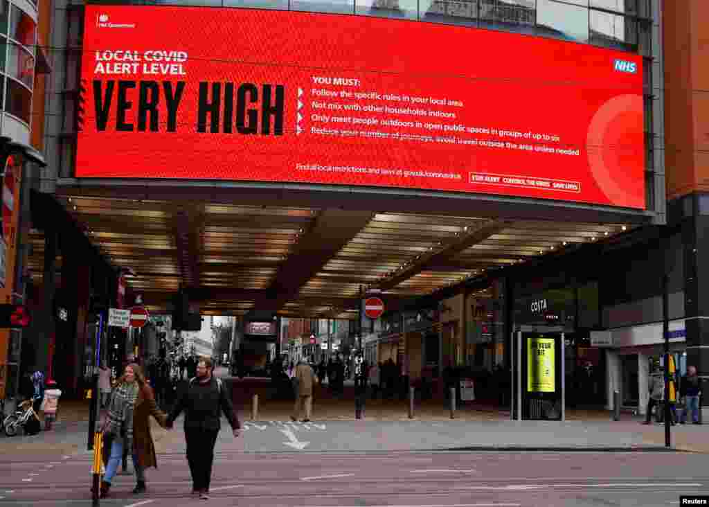 People walk beneath a government information board amid the outbreak of the coronavirus disease (COVID-19) in Manchester, Britain.