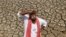 FILE - An Indian farmer looks skyward as he stands on a dried bed of a water body on the outskirts of Ahmadabad, India.
