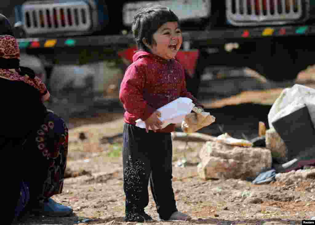 An internally displaced Syrian child reacts as he holds bread at a makeshift refugee camp in Azaz, Syria.