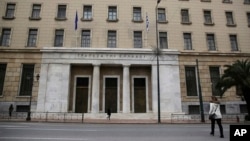 People walk past the Bank of Greece headquarters, in central Athens, March 27, 2015. 