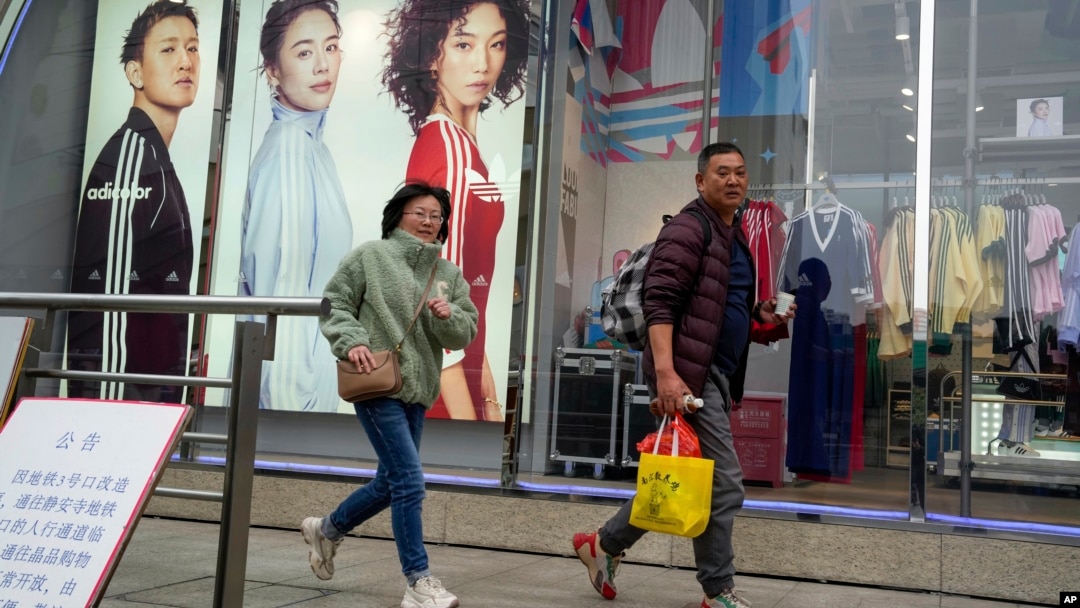 Shoppers walk by an apparel store in Shanghai on March 18, 2024.