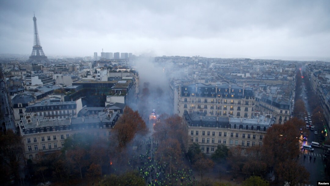 Para pengunjuk rasa mengenakan rompi kuning, simbol protes para pengendara Perancis terhadap kenaikan pajak solar, berdemonstrasi di Place de l'Etoile, Paris dengan latar belakang menara Eiffel, Perancis, 1 Desember 2018. (Foto: dok).