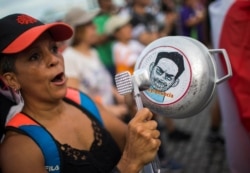 FILE - A demonstrator bangs on a pot that has a cartoon drawing of Governor Ricardo Rossello and text the reads in Spanish "Quit Ricky" in San Juan, Puerto Rico, July 19, 2019.