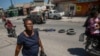ARCHIVO - Una mujer camina junto al cuerpo de un hombre, que yace a mitad de una calle de Puerto Príncipe, el jueves 20 de abril de 2023. 