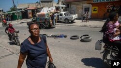 ARCHIVO - Una mujer camina junto al cuerpo de un hombre, que yace a mitad de una calle de Puerto Príncipe, el jueves 20 de abril de 2023. 