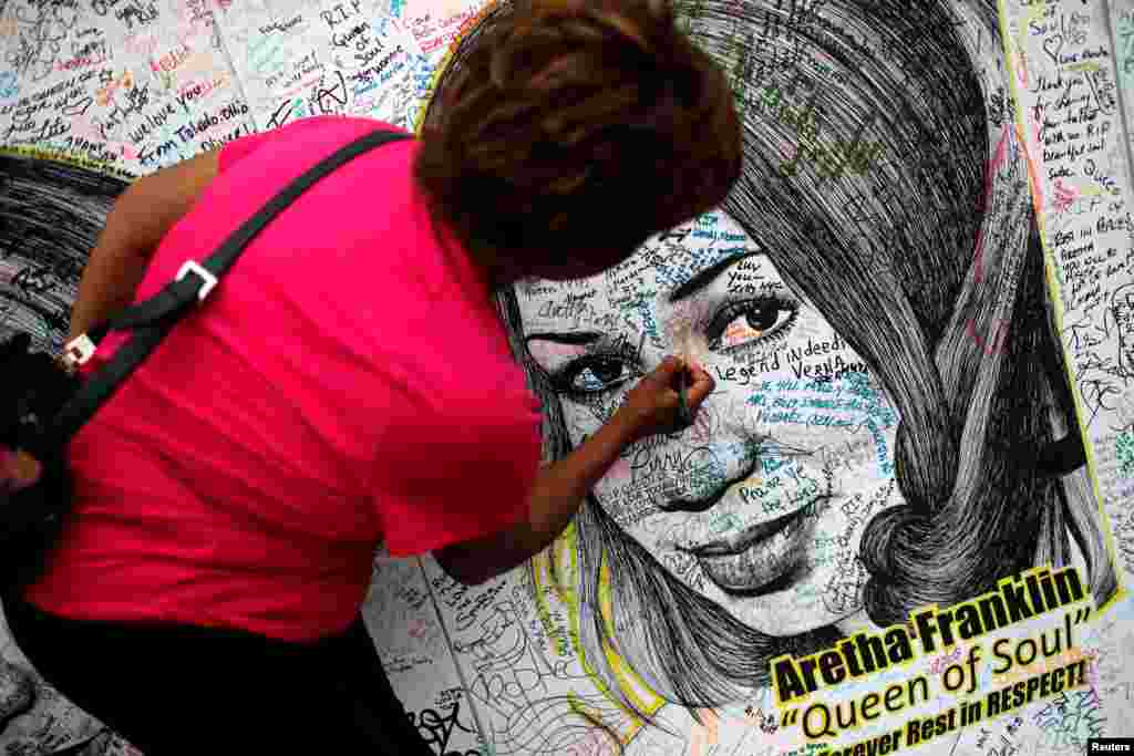 A woman writes on a large drawing of Aretha Franklin outside the Charles H. Wright Museum of African American History on the second day of a public viewing of the late singer in Detroit, Michigan, Aug. 29, 2018.