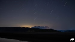 FILE - Stars move on the night sky during the Perseid meteor shower in the Pineios Lake near the village of Velanidi, Peloponnese, Greece, Aug. 13, 2020.