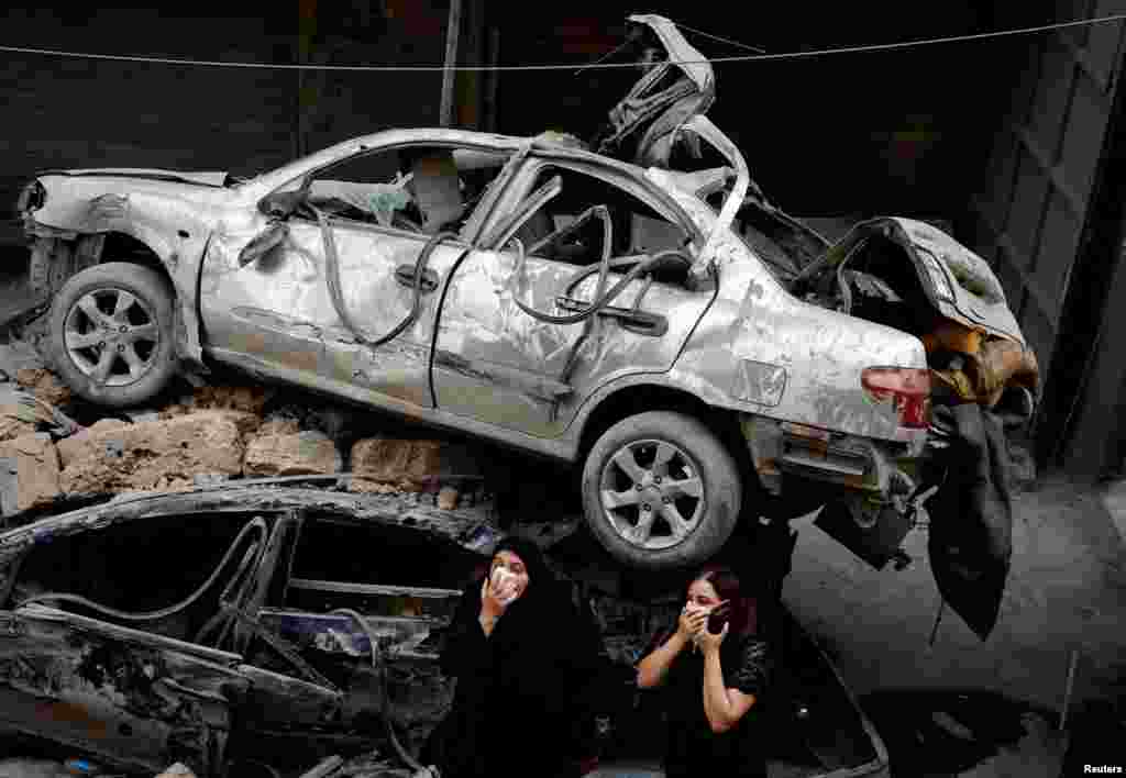 Dua orang perempuan berdiri di samping kendaraan yang rusak di lokasi serangan udara Israel, di tengah pertempuran antara Hizbullah dan pasukan Israel, di Beirut, Lebanon. (Reuters)&nbsp;