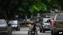 Un hombre, con una mascarilla lleva y que lleva a su perro en su silla de ruedas, pasa entre conductores que hacen fila para cargar combustible en sus vehículos en Caracas, Venezuela, el 9 de mayo de 2021.