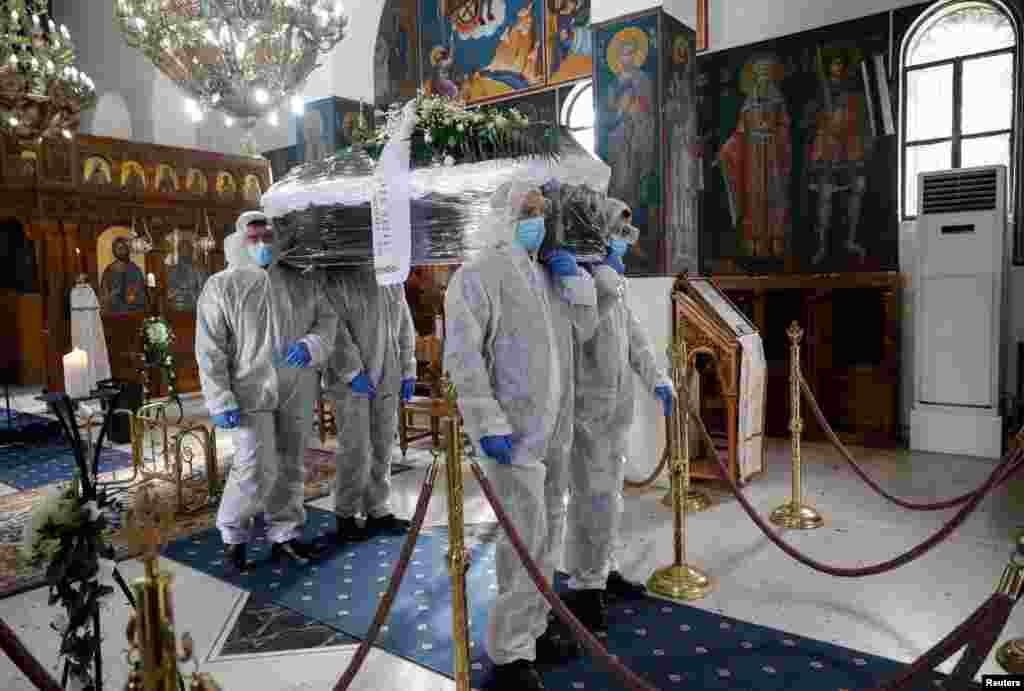 Pallbearers, wearing personal protective equipment (PPE), carry the coffin of a patient who died from COVID-19, inside a church in Athens, Greece.
