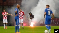 Un pompier débarrasse une grenade fumigène que des supporters ont lancée sur le terrain interrompant momentanément le match de qualification pour l’Euro 2016 entre l'Italie et la Croatie, au stade San Siro à Milan, Italie, 16 novembre 2014. 