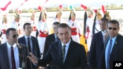 In this handout photo released by the government news agency Agencia Brasil, Brazil's President Jair Bolsonaro, center, talks with reporters outside the presidential official residence Alvorada Palace, in Brasilia, Brazil, Aug. 27, 2019. 