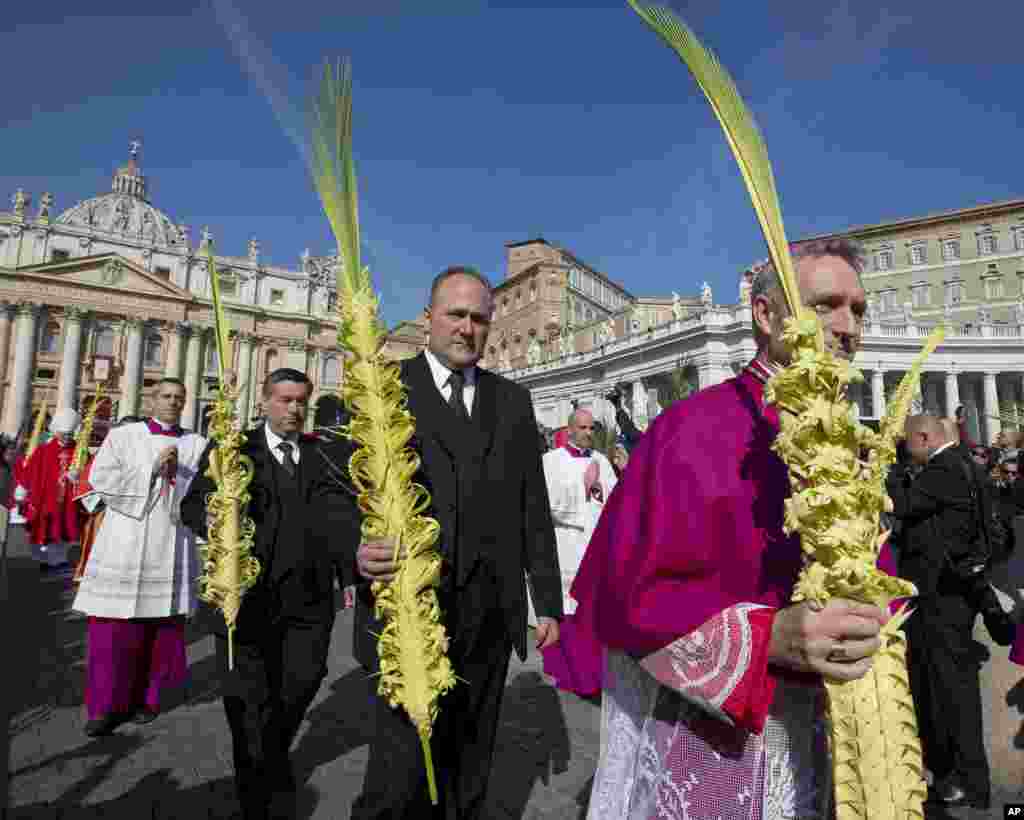 Prefect of the Papal Household Monsignor Georg Gaenswein, right, holds a palm leaf as he walks in procession at the beginning of a Palm Sunday Mass celebrated by Pope Francis, in St. Peter&#39;s Square, at the Vatican.