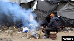 Migrants warm themselves by the fire at a makeshift camp in the transit zone on the Serbian-Hungarian border near Horgos, Serbia, Jan. 9, 2017. 