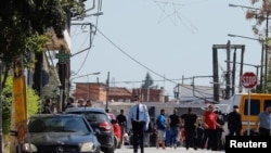 A police officer wearing a protective face mask walks near members of a Roma community where several cases of the coronavirus have been detected, in Larissa, Greece, April 10, 2020.