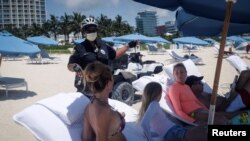 Un policía habla con visitantes de las playas de Miami, Florida, mientras estas reabren con restricciones para evitar la propagación del coronavirus.