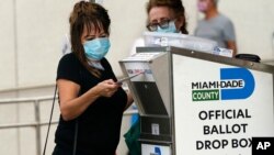 Seorang pekerja pemilu memasukkan kertas suara ke dalam kotak suara resmi di luar lokasi pemungutan suara awal di Miami, Florida, pada 19 Oktober 2020. (Foto: AP)