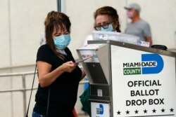 FILE - An election worker places a vote-by-mail ballot into an official ballot drop box outside of an early voting site in Miami, Florida, Oct. 19, 2020.