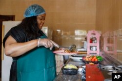 FILE—Anita Akpeere, who uses her mobile phone to run her business, prepares food at her restaurant in Accra, Ghana, April 23, 2024.