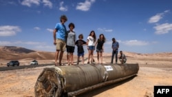 Ljudi stoje na ostacima iranskog projektila u pustinji Negev blizu Arada, 2. oktobra 2024. godine, nakon iranskog raketnog napada na Izrael. (Foto: Menahem Kahana/AFP)