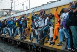 FILE - Train commuters hold on to the side of an overcrowded passenger train in Soweto, South Africa, March 16, 2020.