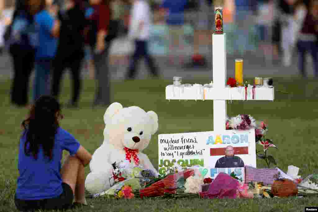 Seorang pelayat duduk di depan sebuah salib yang dihiasi foto-foto para korban, dengan bunga-bunga dan cendera mata, di tempat peringatan, dua hari setelah insiden penembakan di SMU Marjory Stoneman Douglas, di Parkland, Florida, 16 Februari 2018.