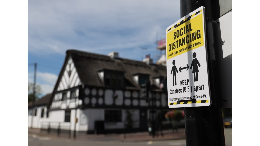 FILE - A sign promoting social distancing is hung on a post near the Crown and Anchor pub following a spike in cases of COVID-19 to visitors of the pub in Stone, Britain, July 30, 2020.