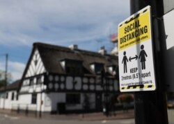 FILE - A sign promoting social distancing is hung on a post near the Crown and Anchor pub following a spike in cases of COVID-19 to visitors of the pub in Stone, Britain, July 30, 2020.