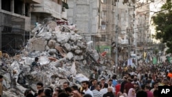 جمعی از فلسطینیان ساکن غزه، پس از برقراری آتش‌بس میان اسرائیل و حماس، از کنار خرابه‌های یک ساختمان که در حمله هوایی اسرائیل به شهر غزه تخریب شده بود، عبور می‌کنند. جمعه ٣١ اردیبهشت ۱۴۰۰ (منبع: آسوشیتدپرس)