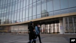 People wearing protective face masks walk by a quiet Silk Street Mall, a usually popular tourist spot before the new coronavirus outbreak in Beijing, March 11, 2020. 