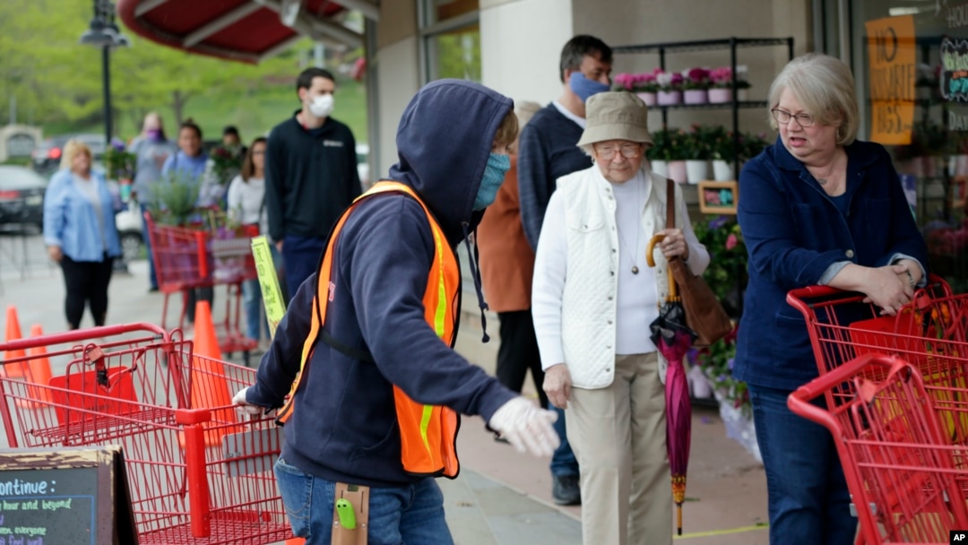 Doorman Dilon Moore, center, helps with shopping carts and controls the number of customers allowed to shop at one time at a Trader Joe's supermarket in Omaha, Neb., May 7, 2020. 