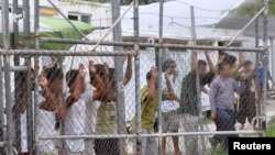 FILE - Asylum-seekers look through a fence at the Manus Island detention center in Papua New Guinea, March 21, 2014. 