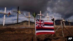 FILE - A Hawaiian flag and crosses honoring the victims killed in a recent wildfire are posted along the Lahaina Bypass in Lahaina, Hawaii, Aug. 21, 2023. 