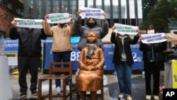 FILE - Protesters hold banners during a rally to mark the March First Independence Movement Day against Japanese colonial rule, in front of a statue symbolizing a wartime sex slave, near Japan's embassy in Seoul, South Korea, March 1, 2021.