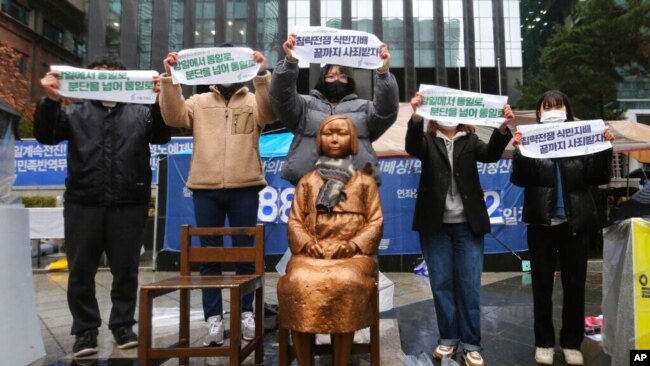 FILE - Protesters hold banners during a rally to mark the March First Independence Movement Day against Japanese colonial rule, in front of a statue symbolizing a wartime sex slave, near Japan's embassy in Seoul, South Korea, March 1, 2021.