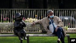 A man relaxes on a bench in London, next to a sculpture of Paddington Bear, as the country is in lockdown to help curb the spread of the coronavirus, April 15, 2020. 