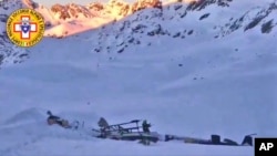 A rescuer stands next to the debris of a helicopter after a midair collision between the aircraft and a small tourist airplane in the northwestern Italian region of Val d'Aosta, Jan 25, 2019. 