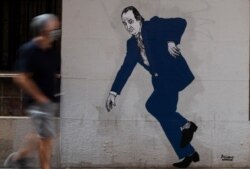 A man wearing a face mask walks past a graffiti by artist El Primo de Bansky of former Spanish King Juan Carlos in a street of Valencia, on Aug. 6, 2020.