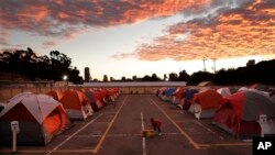 FILE - A boy plays as the sun sets over donated tents for homeless families lined up on a parking lot in the city-sanctioned encampment in San Diego, Nov. 8, 2017. A parking lot in San Diego's famed Balboa Park has acted for the past two months as an unusual triage center. Scores of tents, mobile medical units, portable toilets and showers were brought in to meet the needs of hundreds of people affected by a societal problem that has bloomed into a deadly disaster: homelessness.