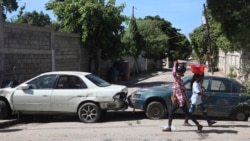 Pejalan kaki berjalan melewati kendaraan yang berfungsi sebagai barikade yang didirikan warga untuk mencegah anggota geng memasuki lingkungan mereka, di pusat kota Port-au-Prince, Haiti, Rabu, 13 November 2024. (Foto: AP)