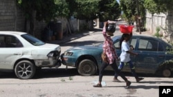 Dos personas caminan cerca de vehículos estacionados como parte de una barricada de miembros de una comunidad residencial en Puerto Príncipe, Haití, el 13 de noviembre de 2024. (AP/Odelyn Joseph)