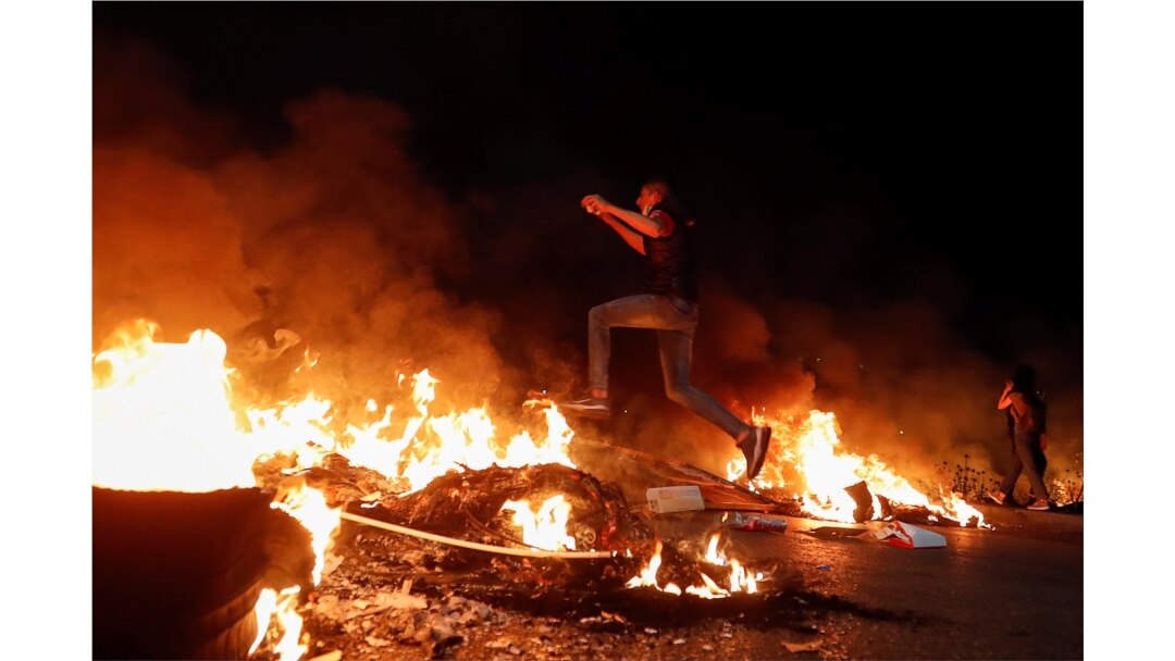 Seorang demonstran Palestina melompati barikade yang terbakar selama protes anti-Israel atas ketegangan di Yerusalem, dekat pemukiman Yahudi Beit El dekat Ramallah, di Tepi Barat yang diduduki Israel, 9 Mei 2021. (Foto: Reuters)