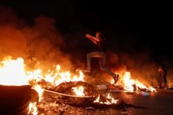 Seorang demonstran Palestina melompati barikade yang terbakar selama protes anti-Israel atas ketegangan di Yerusalem, dekat pemukiman Yahudi Beit El dekat Ramallah, di Tepi Barat yang diduduki Israel, 9 Mei 2021. (Foto: Reuters)