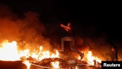 A Palestinian demonstrator jumps over a burning barricade during an anti-Israel protest over tension in Jerusalem, near the Jewish settlement of Beit El near Ramallah, in the Israeli-occupied West Bank, May 9, 2021. 