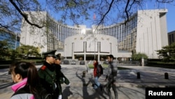 FILE - People walk past the headquarters of the People's Bank of China as two police officials patrol the area in Beijing Nov. 20, 2013. 