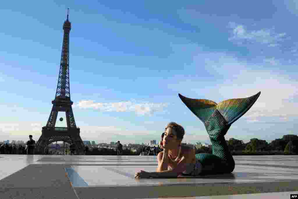 A model dressed as a mermaid poses in front of the Eiffel Tower during sunrise in Paris.