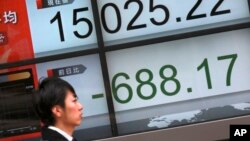 People walk past an electronic stock board showing Japan's Nikkei 225 in Tokyo, Friday, Feb. 12, 2016.