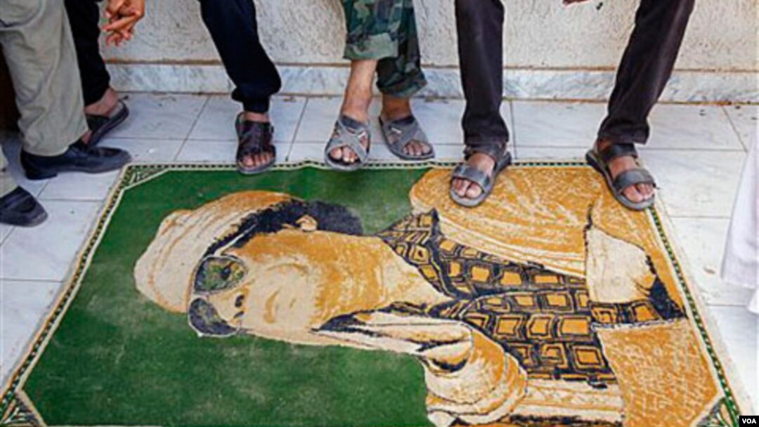 Los rebeldes libios usan de alfombra una imágen de Moammar Gadhafi, a la entrada del campamento en Tarhouna.