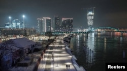 FILE - People walk on the banks of Sava river as the Belgrade Waterfront project is seen under construction in the background, in Belgrade, Serbia, Jan. 17, 2021. 