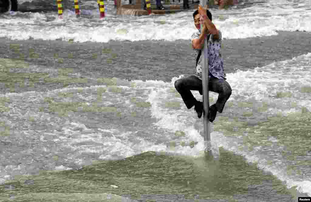 A man climbs on a road sign pole to escape the water from a tidal bore which surged past a barrier on the banks of Qiantang River, in Hangzhou, Zhejiang province, China, Sept. 1, 2015.